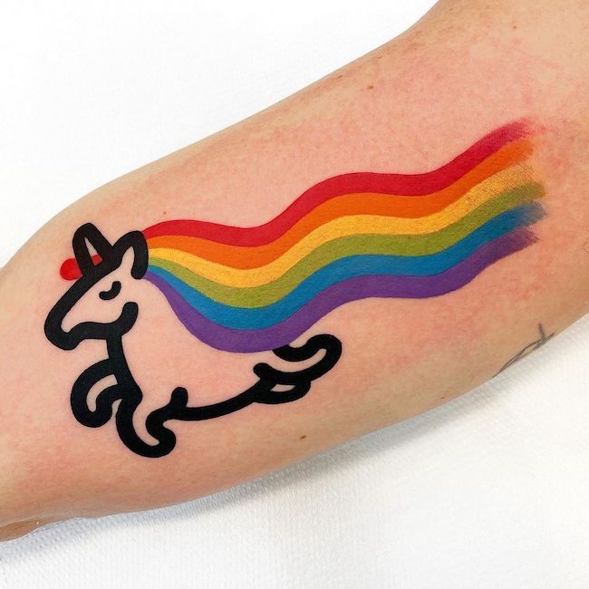 Un atrevido tatuaje de arcoíris y unicornio en el brazo diseñado por @mambotattooer
